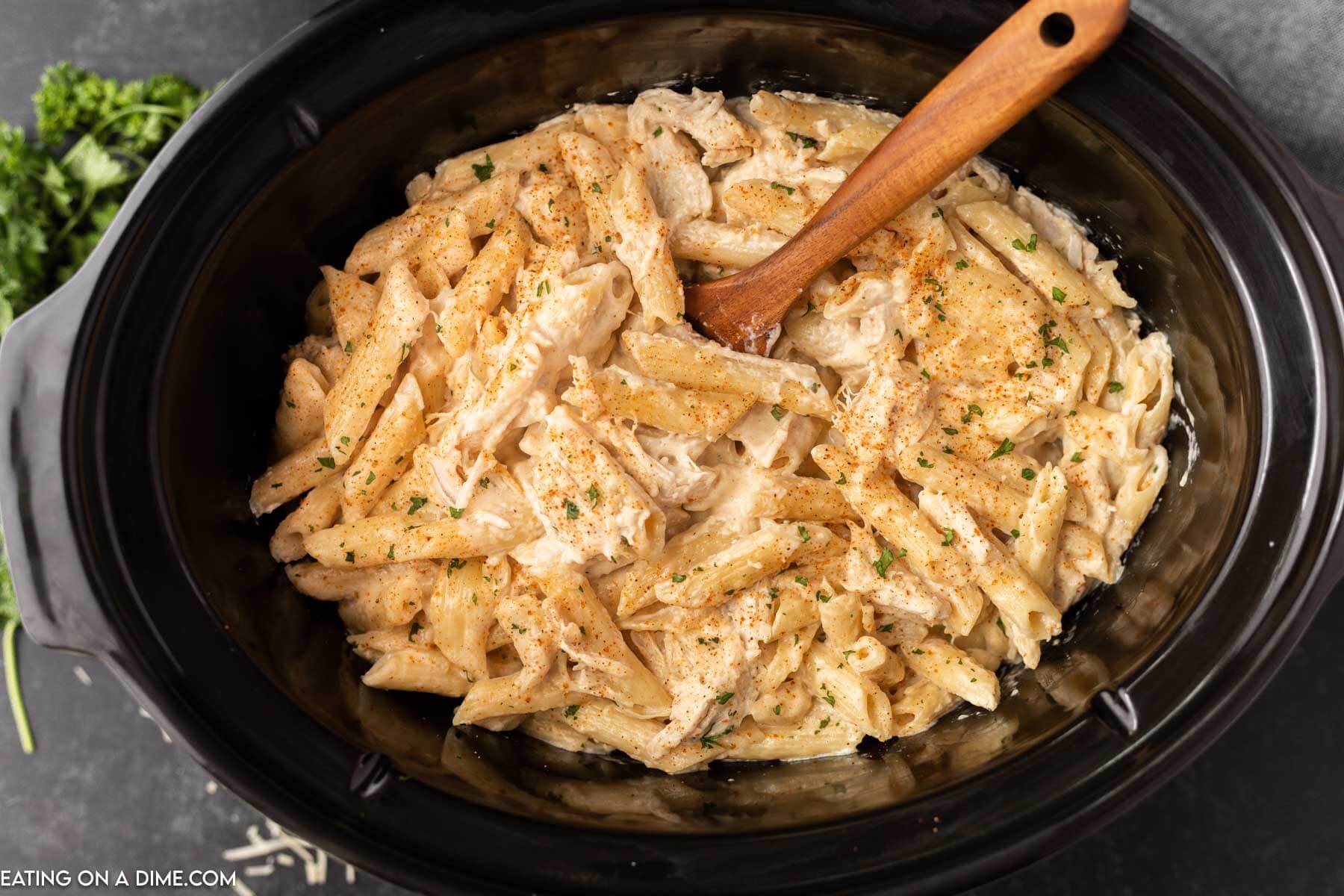 Cajun chicken pasta in the slow cooker with a wooden spoon