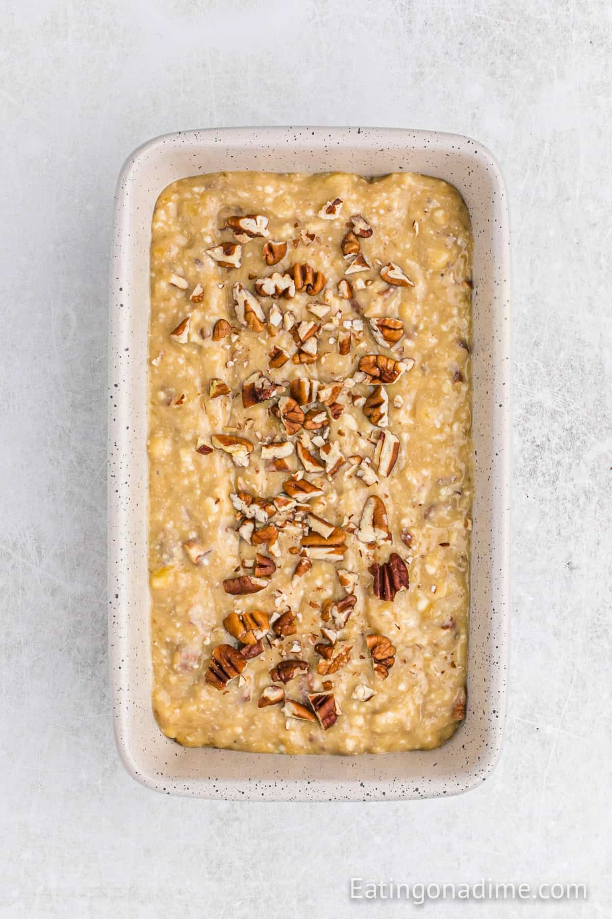 Banana bread batter added to the loaf pan and topped with chopped pecans.