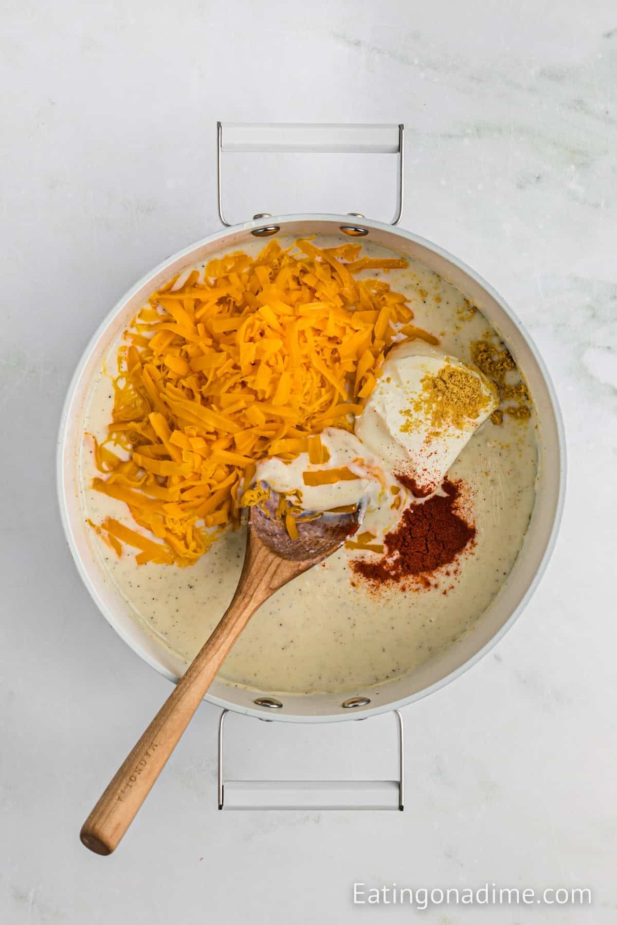 Shredded cheese, spices, cream cheese and milk added to the chopped onions in the large pot with a wooden spoon.