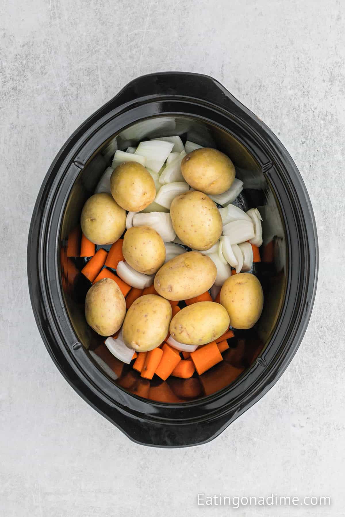 Potatoes, carrots and onions added to the slow cooker.
