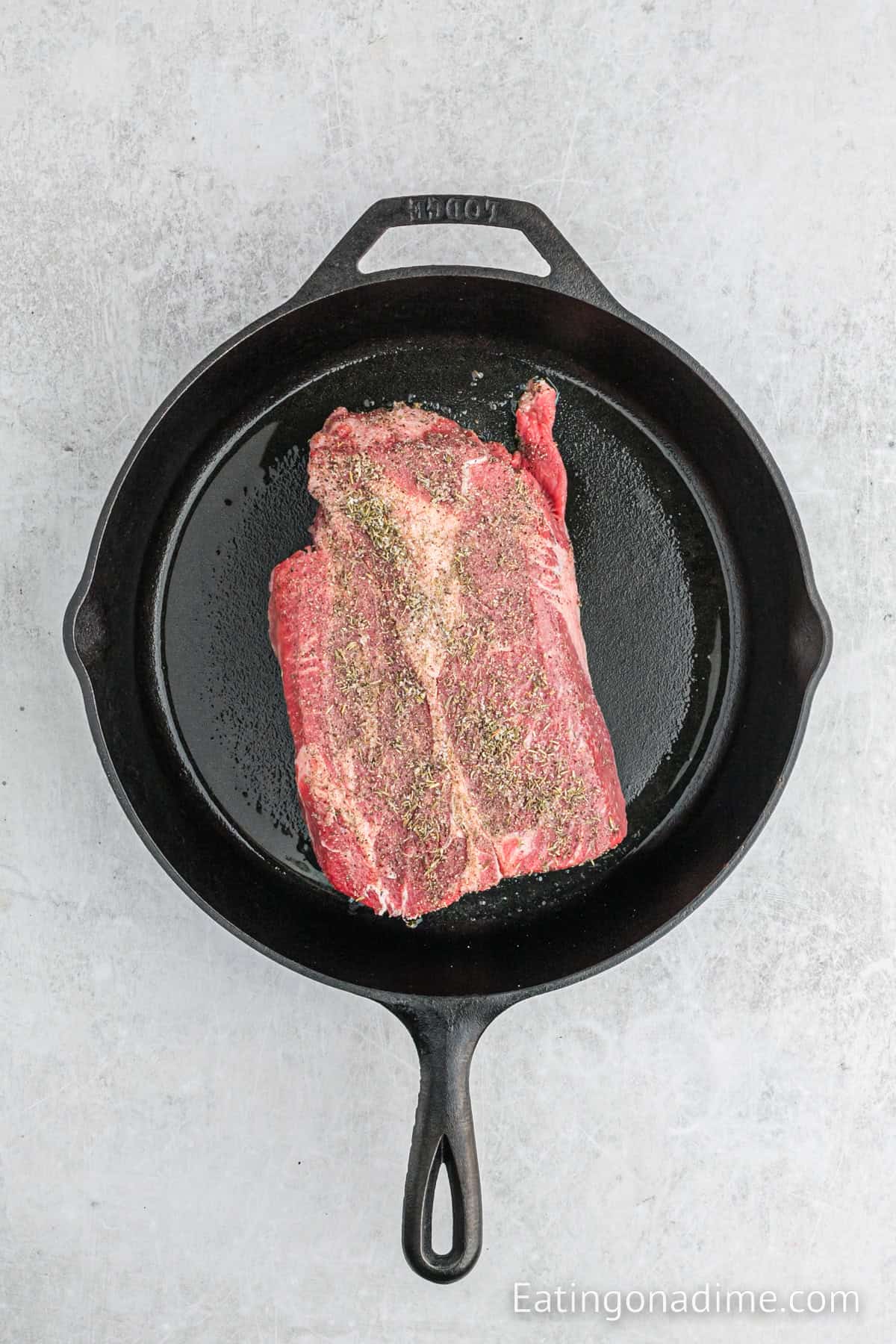 Uncooked roast in a cast iron skillet topped with seasoning.