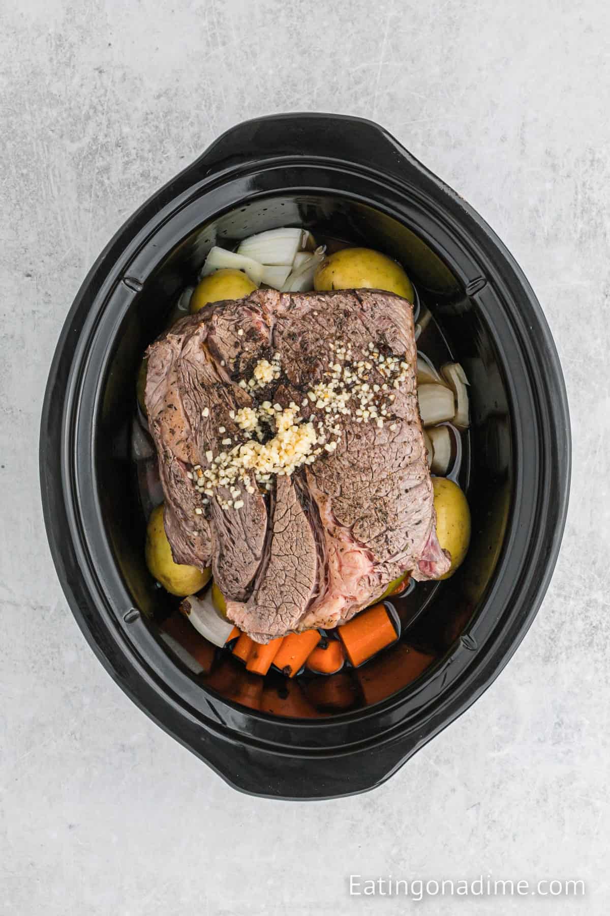Seared roast placed on top of the vegetables in the slow cooker. Minced garlic, broth and worcestershire is added to the crockpot.