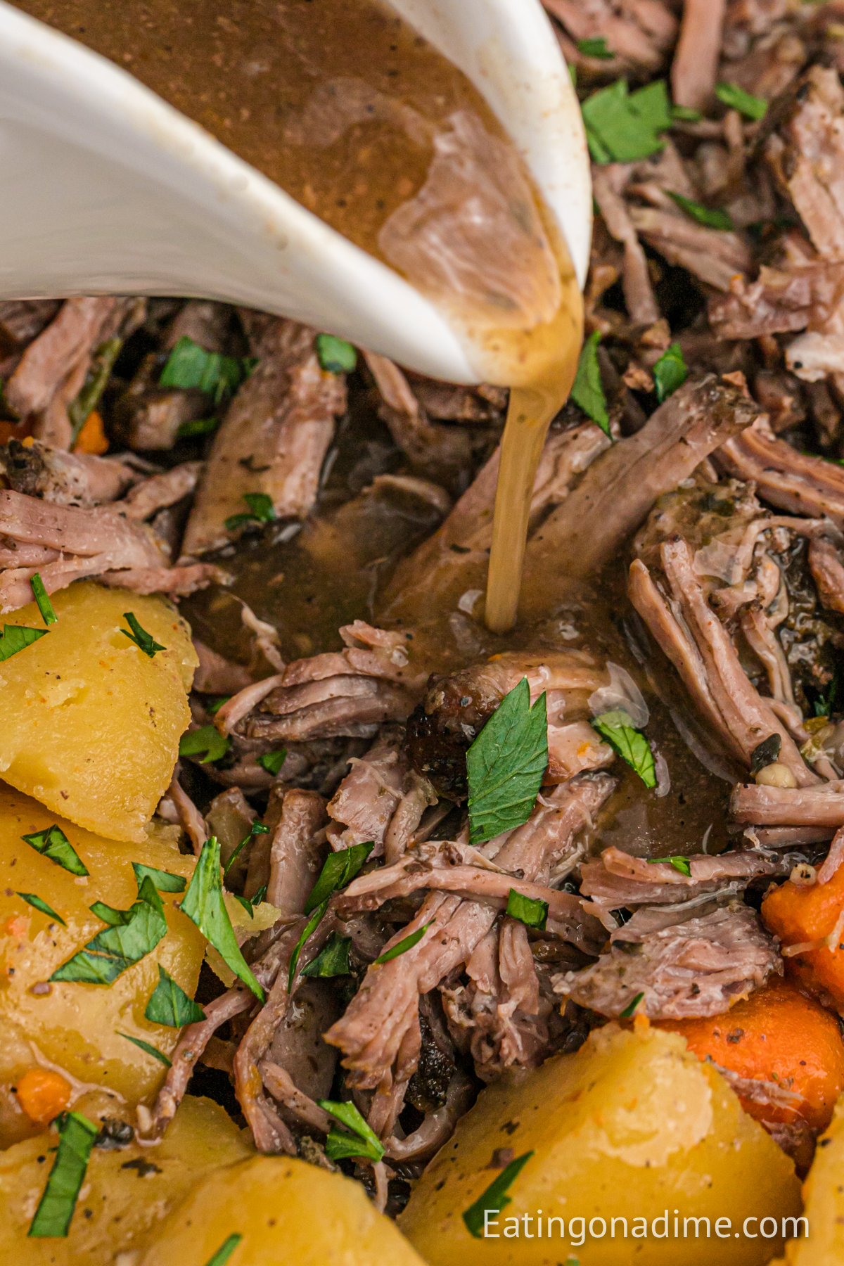 Shred Pot Roast on a platter with potatoes and carrots with gravy being poured over it