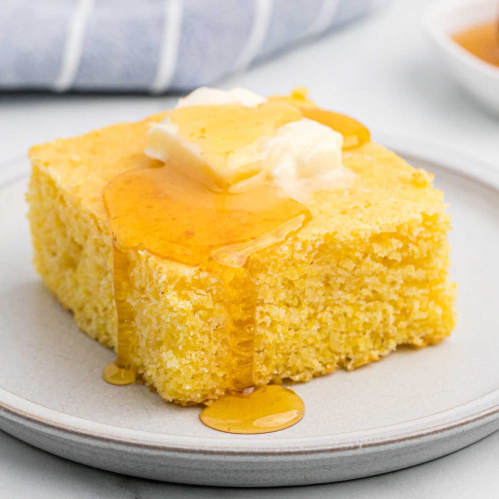 A slice of cornbread on a plate with syrup and butter on top.