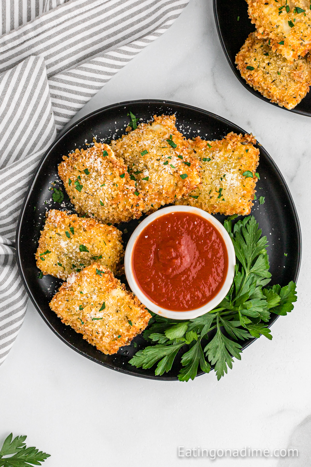 Close up image of toasted ravioli on a plate with a bowl of marinara sauce