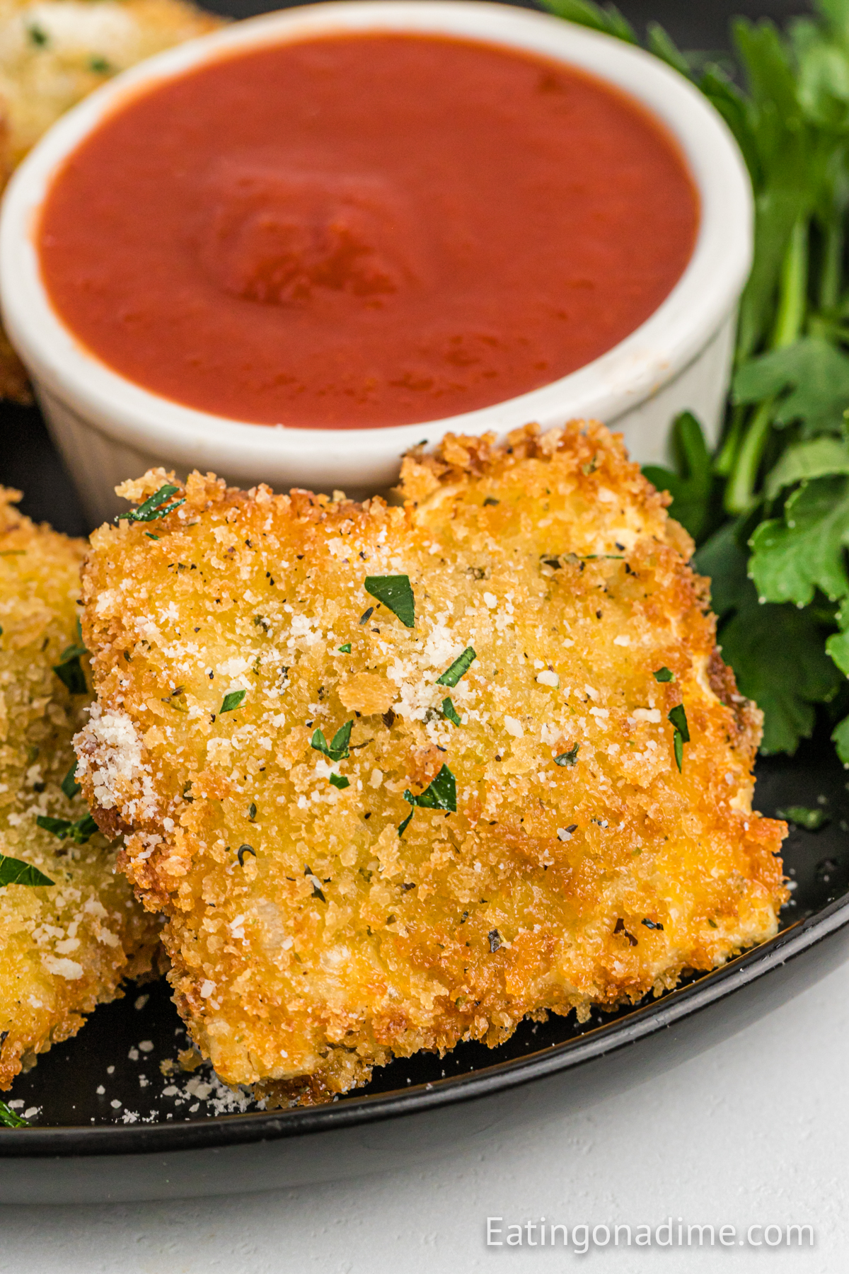 Close up image of toasted ravioli on a plate with a bowl of marinara sauce