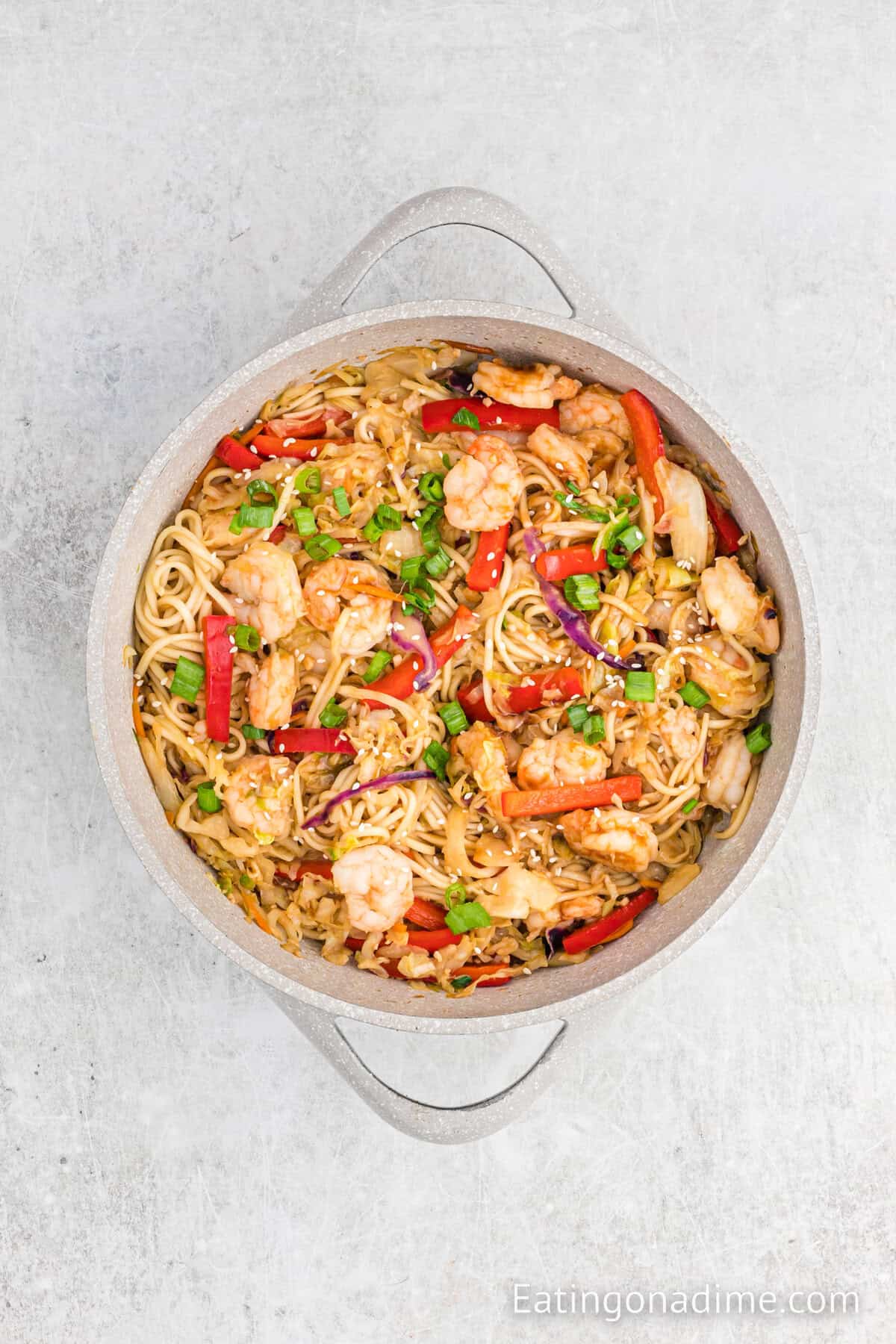 Cooked shrimp, noodle and veggies topped with chopped green onions in a large skillet.