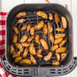 Crispy, golden brown potato wedges sit in an air fryer basket alongside delightful slices of air fryer apples. A red and white checkered cloth is partially visible next to the air fryer on the left.