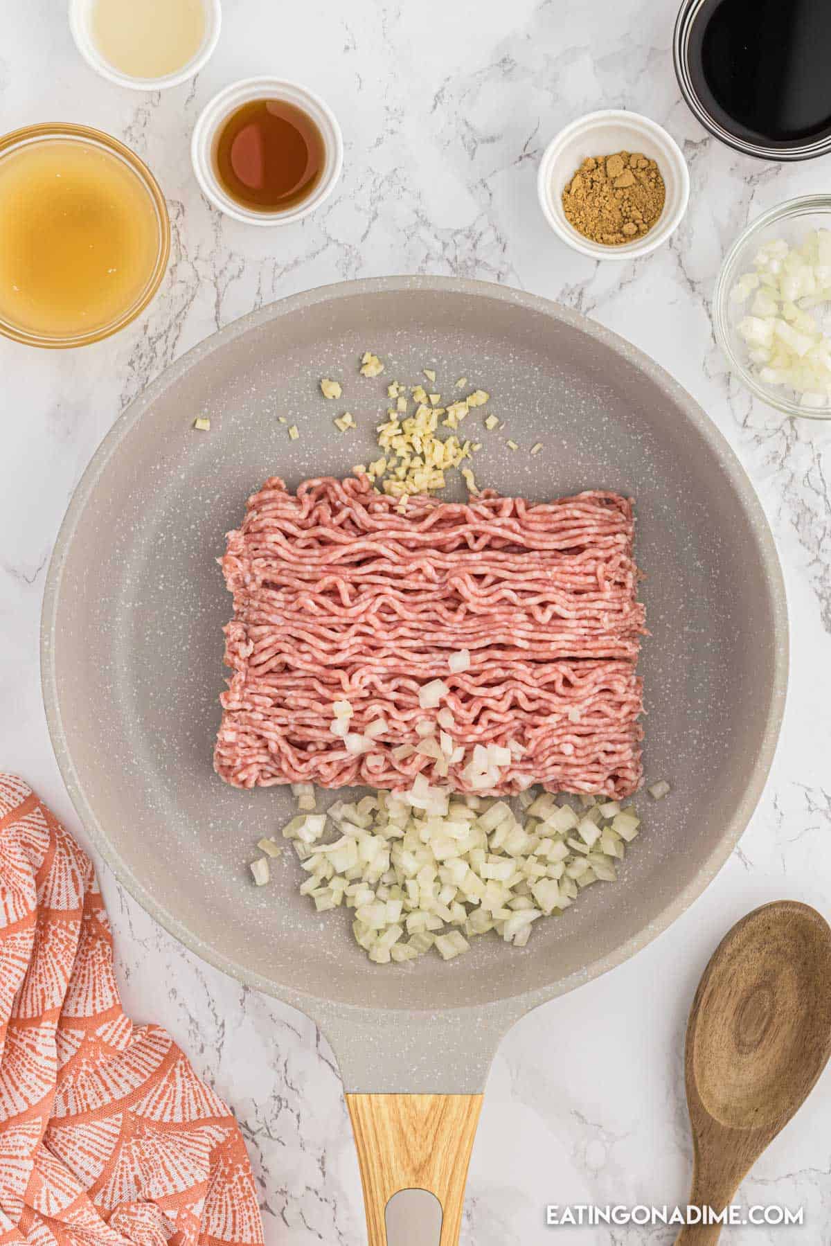Cooking ground turkey in a skillet with chopped onions and minced garlic with small bowls of sauce and seasoning on the side
