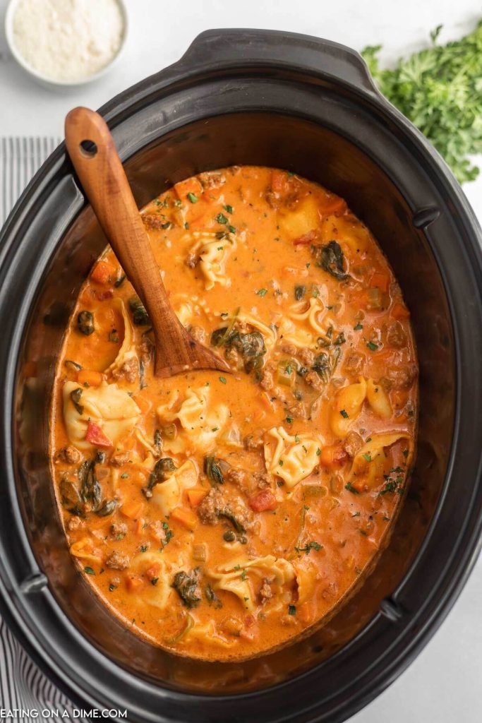 Close up image of creamy sausage tortellini soup in a slow cooker with a wooden spoon
