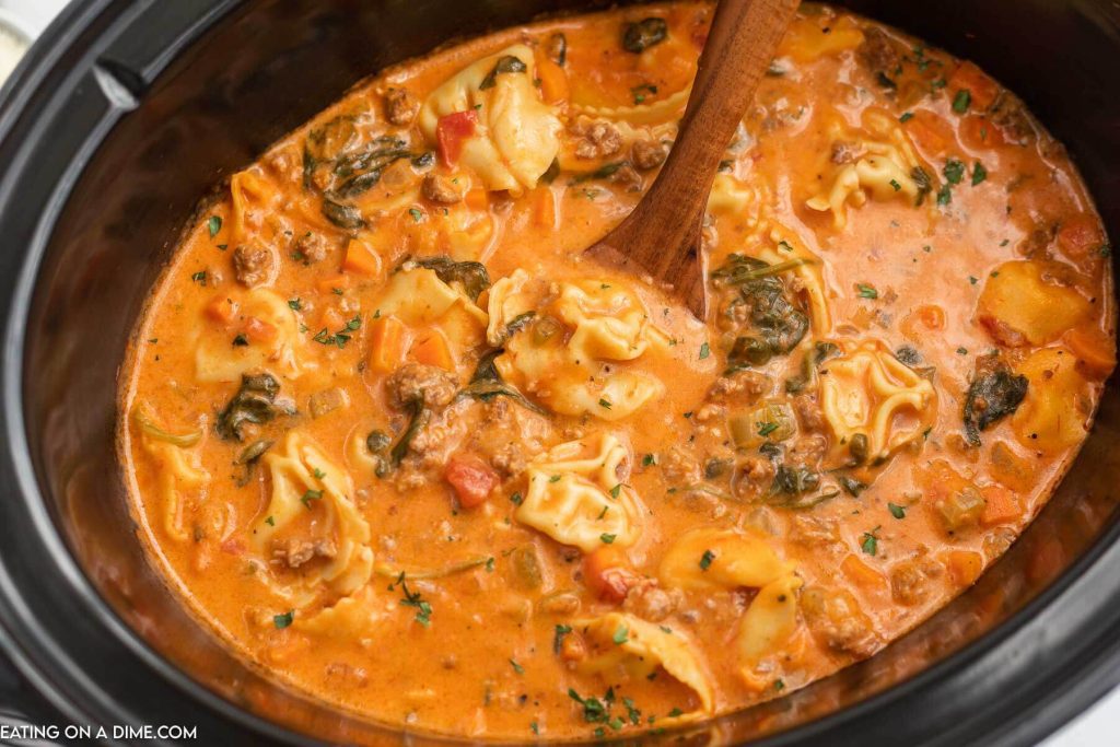Close up image of creamy sausage tortellini soup in the crock pot with a wooden spoon