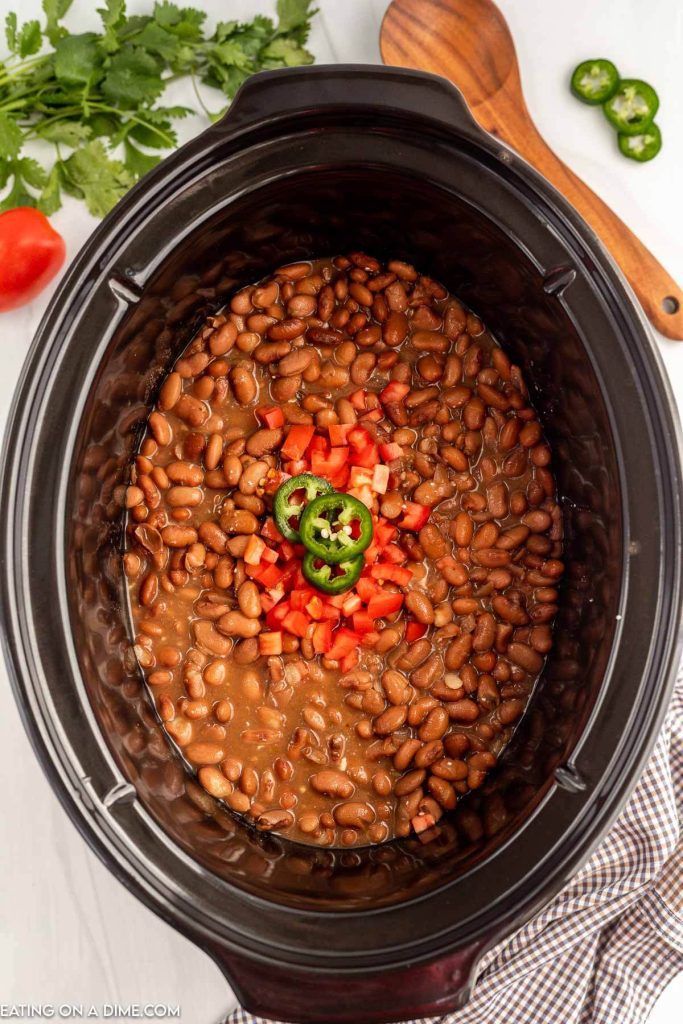 slow cooker of pinto beans topped with fresh tomatoes and sliced jalapenos 