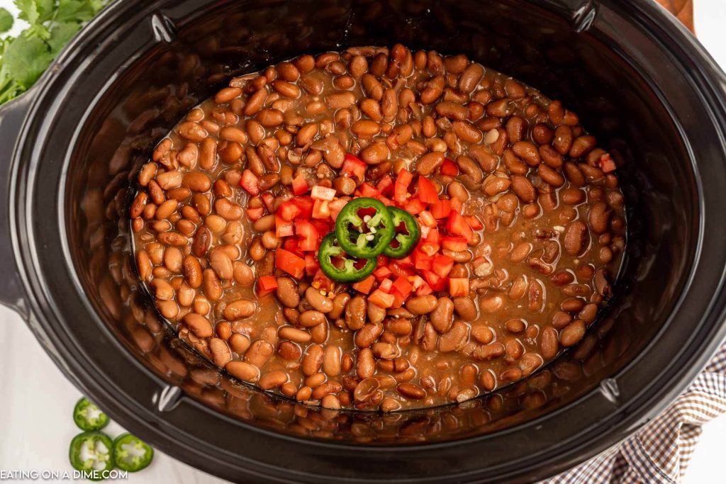 slow cooker of pinto beans topped with fresh tomatoes and sliced jalapenos 