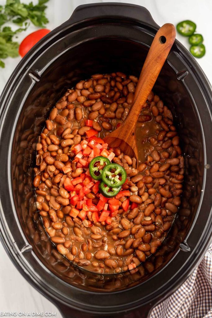 Slow Cooker pinto beans topped with fresh tomatoes and sliced jalapenos with a wooden spoon