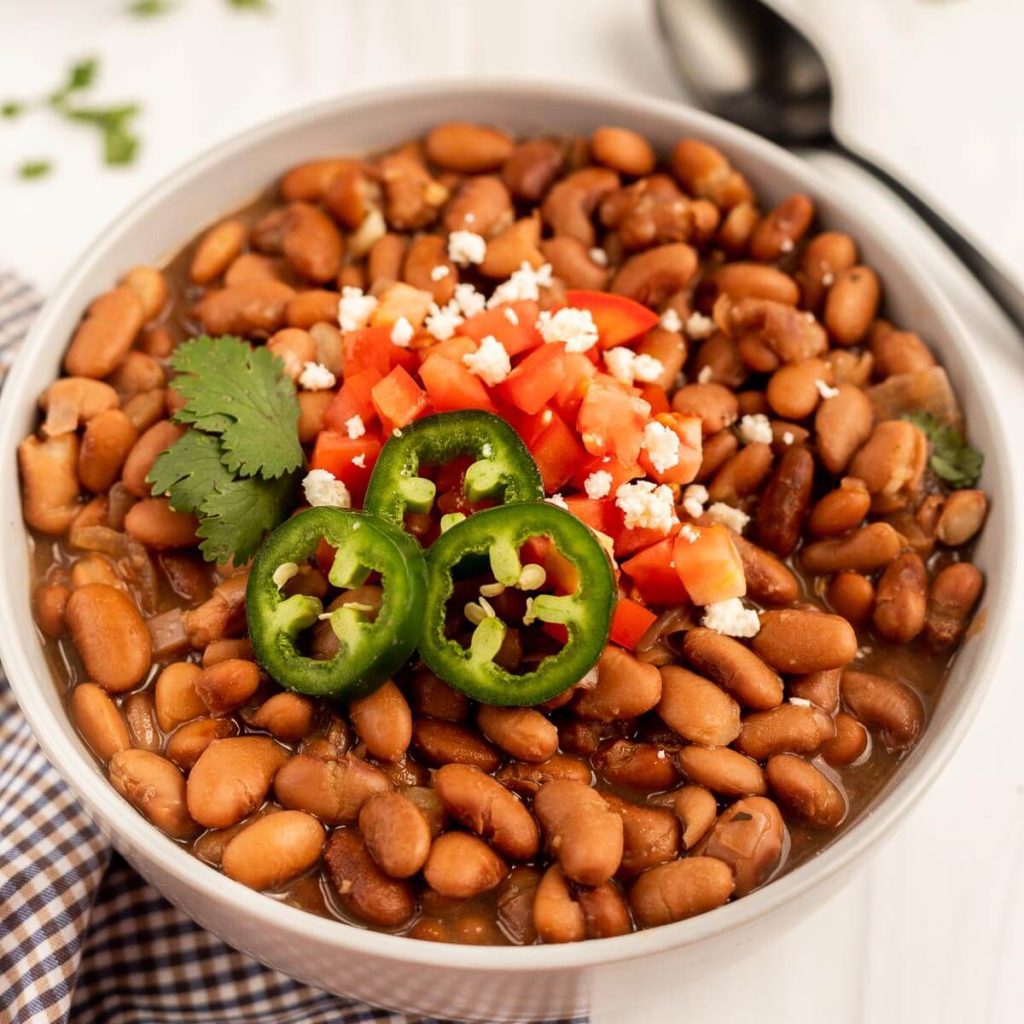 a bowl of pinto beans topped with fresh tomatoes and sliced jalapenos 