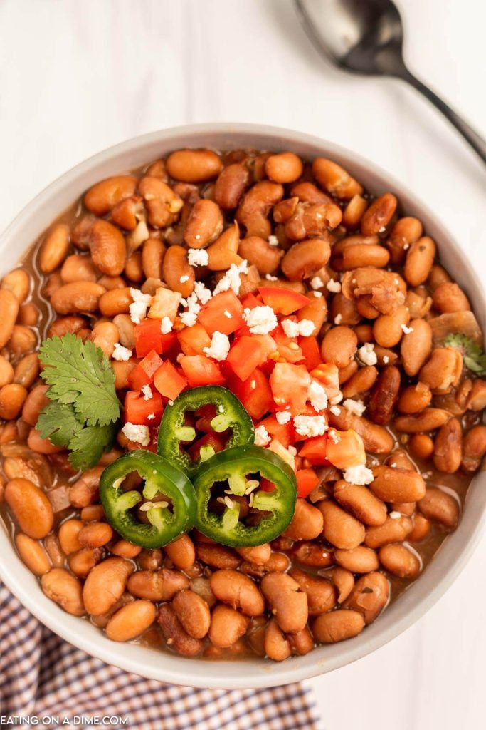 a bowl of pinto beans topped with fresh tomatoes and sliced jalapenos 