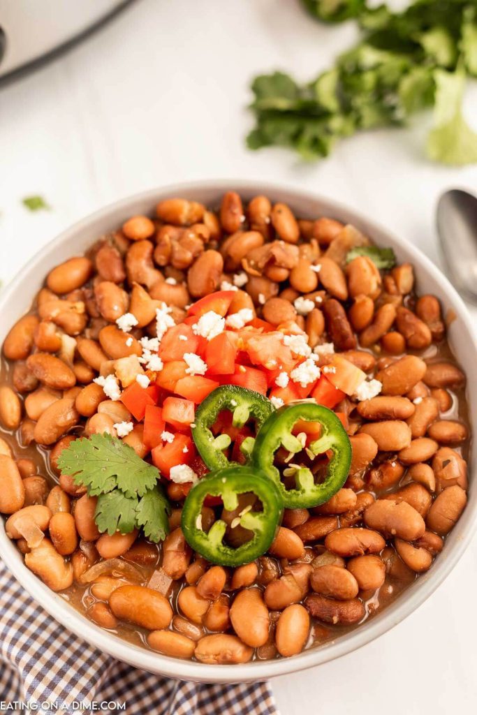 a bowl of pinto beans topped with fresh tomatoes and sliced jalapenos 