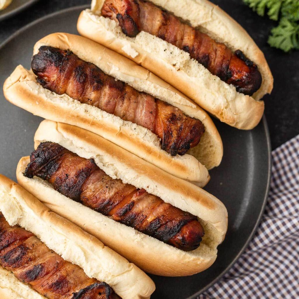 Bacon wrapped hot dogs on a plate. 