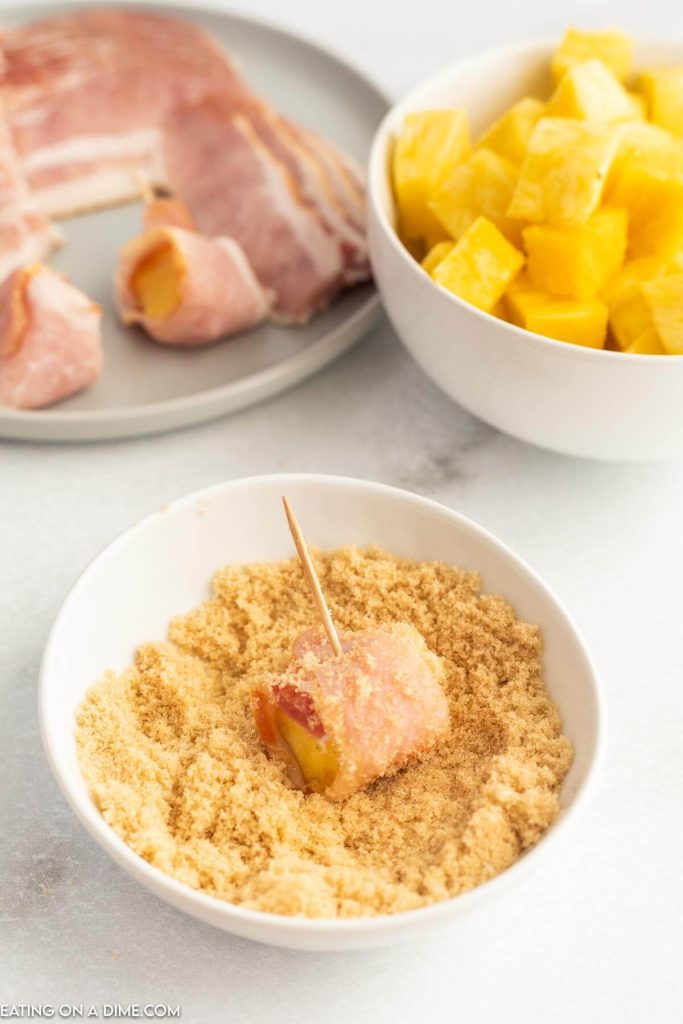 Dipping the bacon wrapped pineapple in brown sugar