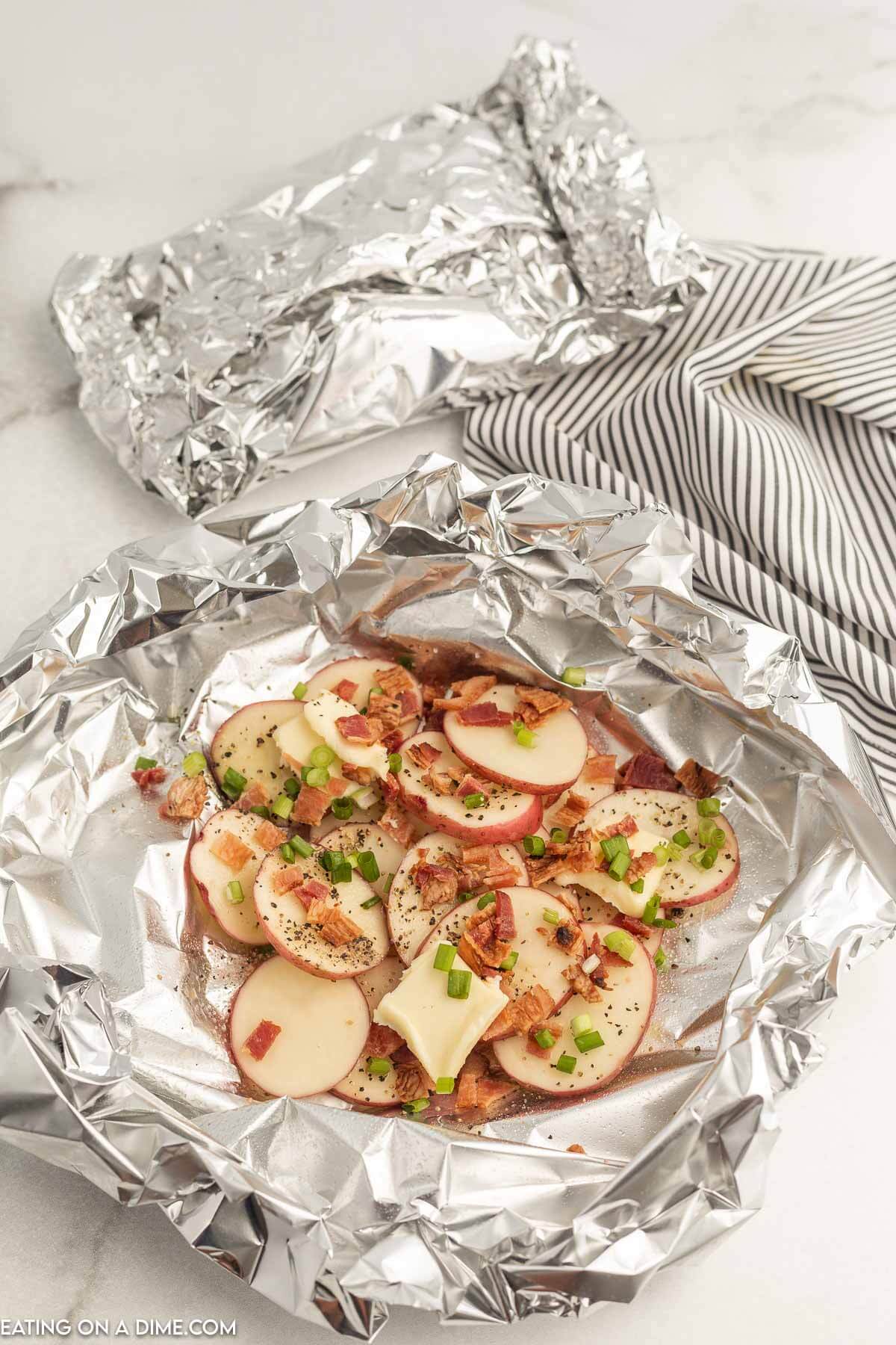 Loading foil with slice potatoes and topping with bacon green onions and seasoning