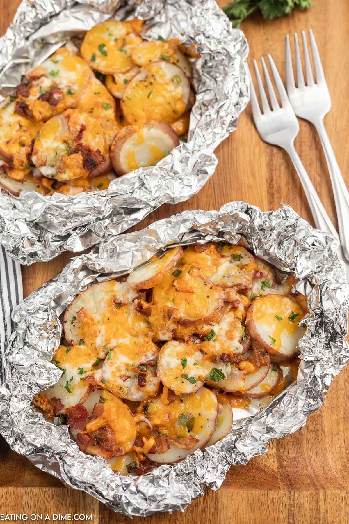 Campfire Potatoes in foil topped with melted cheese, chopped bacon and fresh herbs