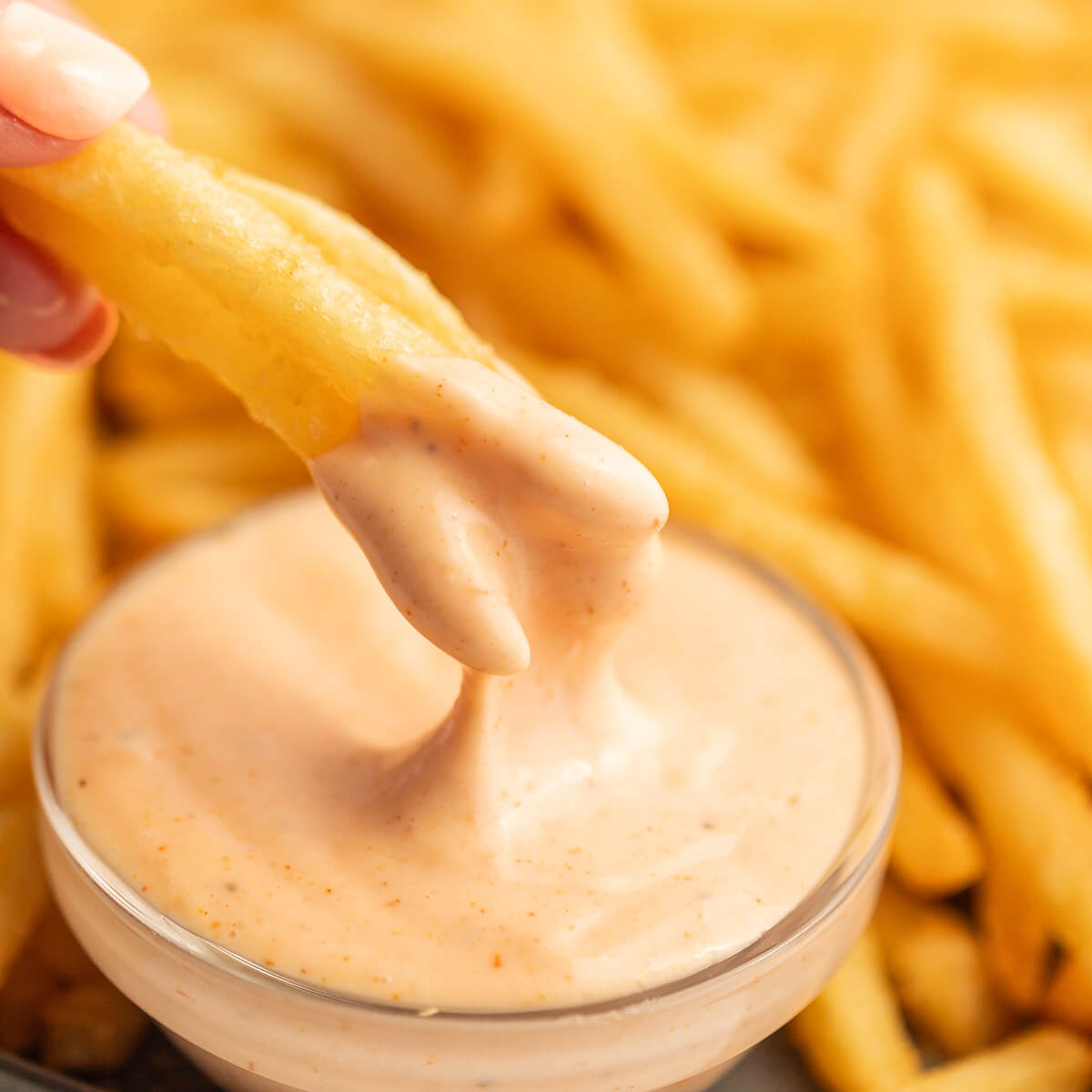 French fries being dipped in fry sauce with a plate of french fries