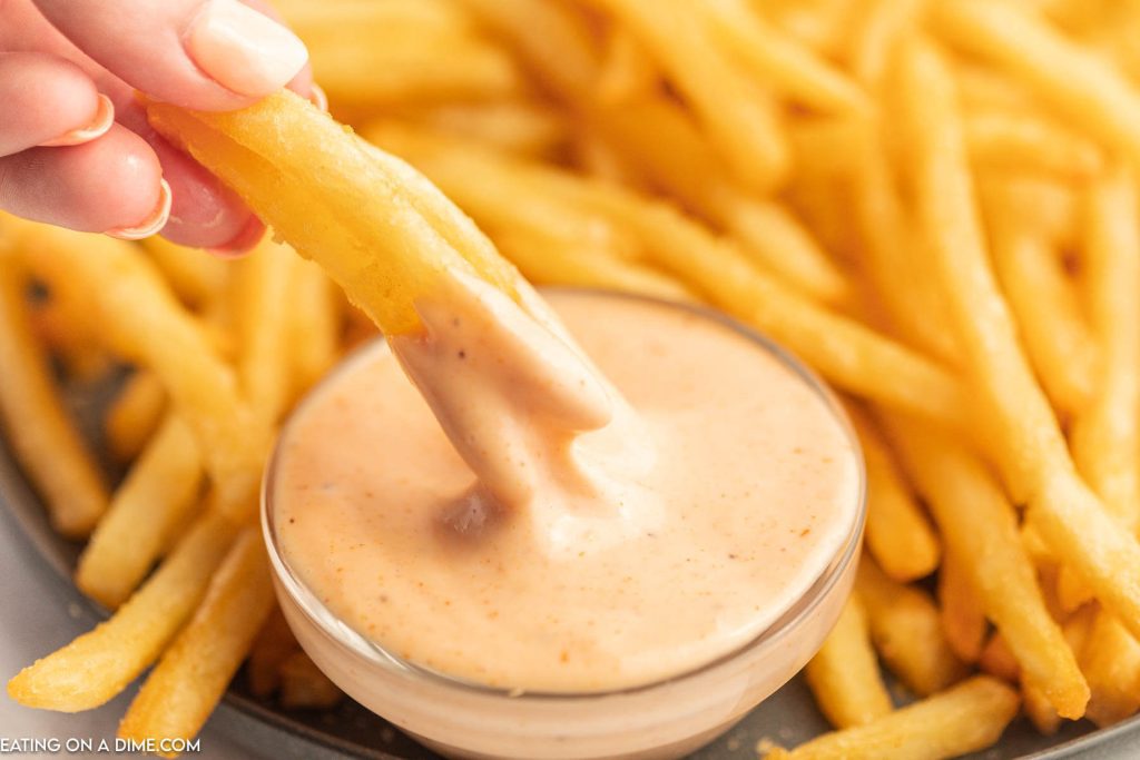 French fries being dipped in fry sauce with a plate of french fries