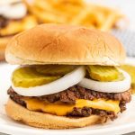 Cheeseburger topped with slice pickles and onions on a plate.