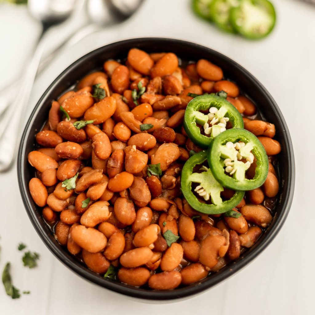 Close up image of a bowl of pinto beans topped with sliced jalapenos