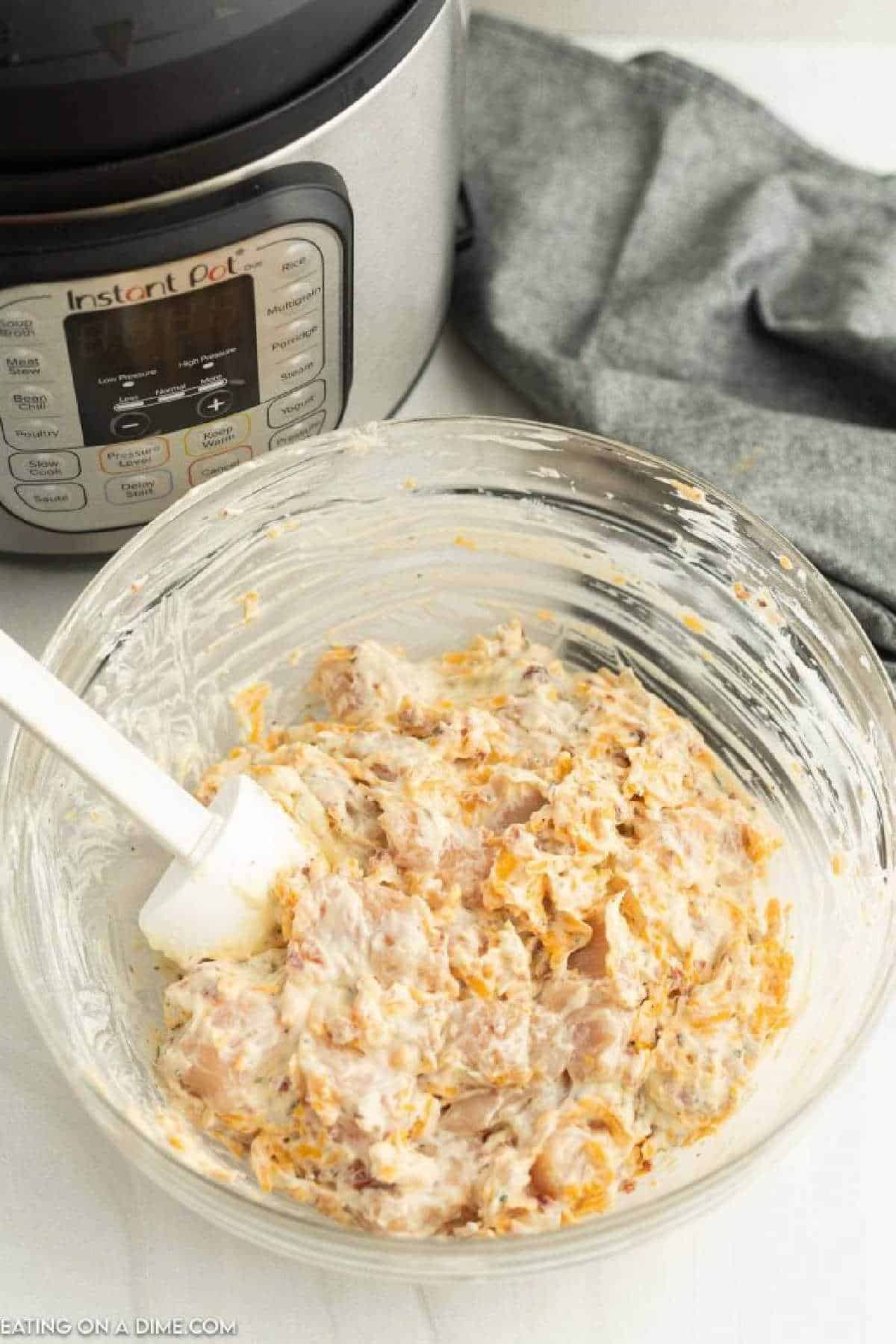 Mixing the ingredients for crack chicken in a clear bowl with a spatula.