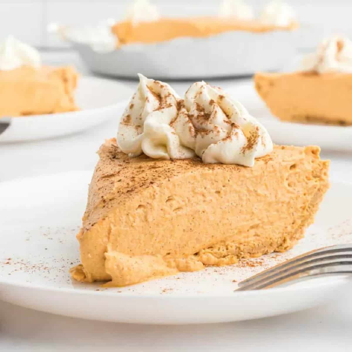 Slice of no bake pumpkin pie on a plate topped with whipped cream.