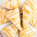 A plate of glazed, triangular scones inspired by the Starbucks Pumpkin Scones Recipe, arranged in a circle and each topped with a shiny icing drizzle.