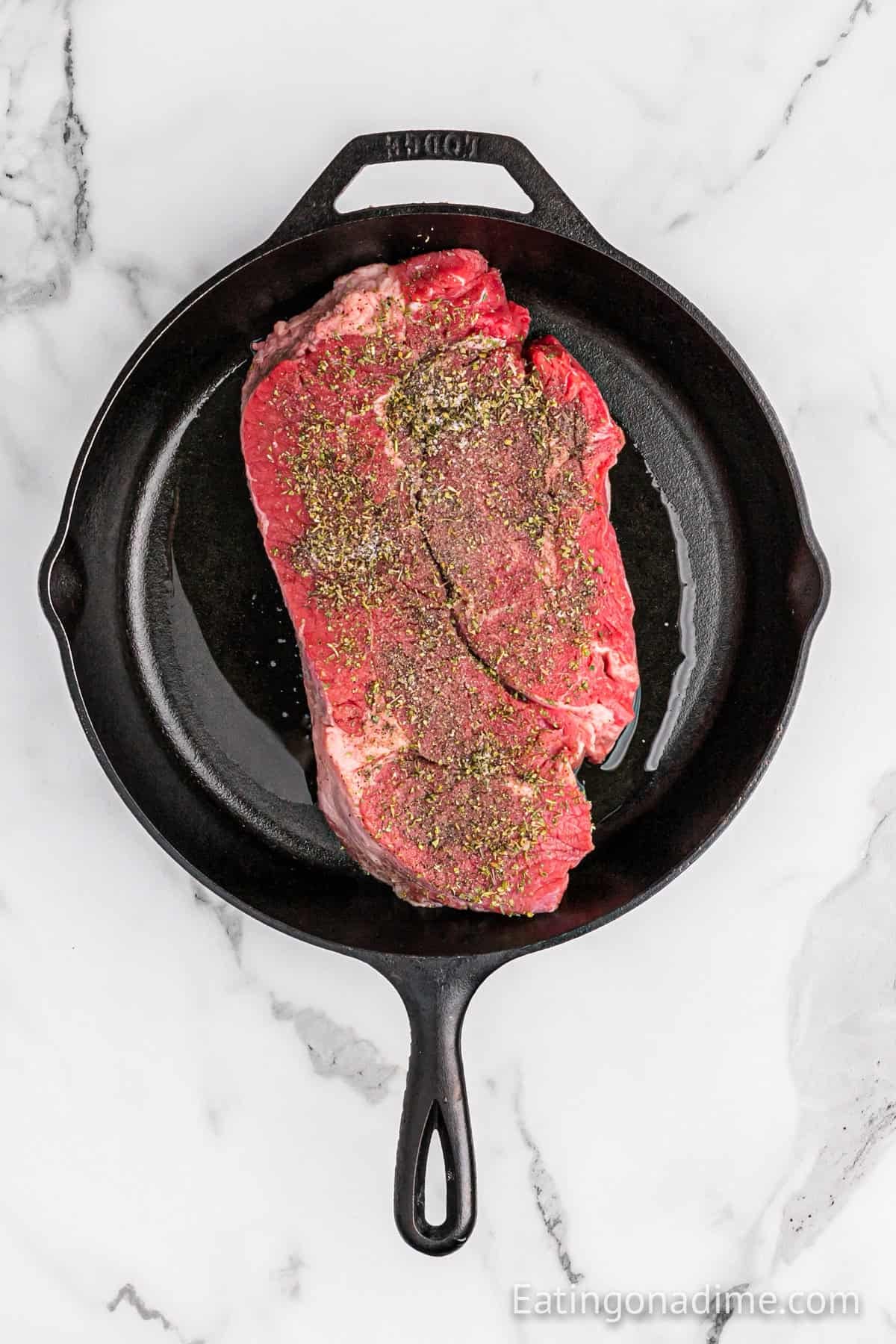 Uncooked roast topped with seasoning in a oiled cast iron skillet.