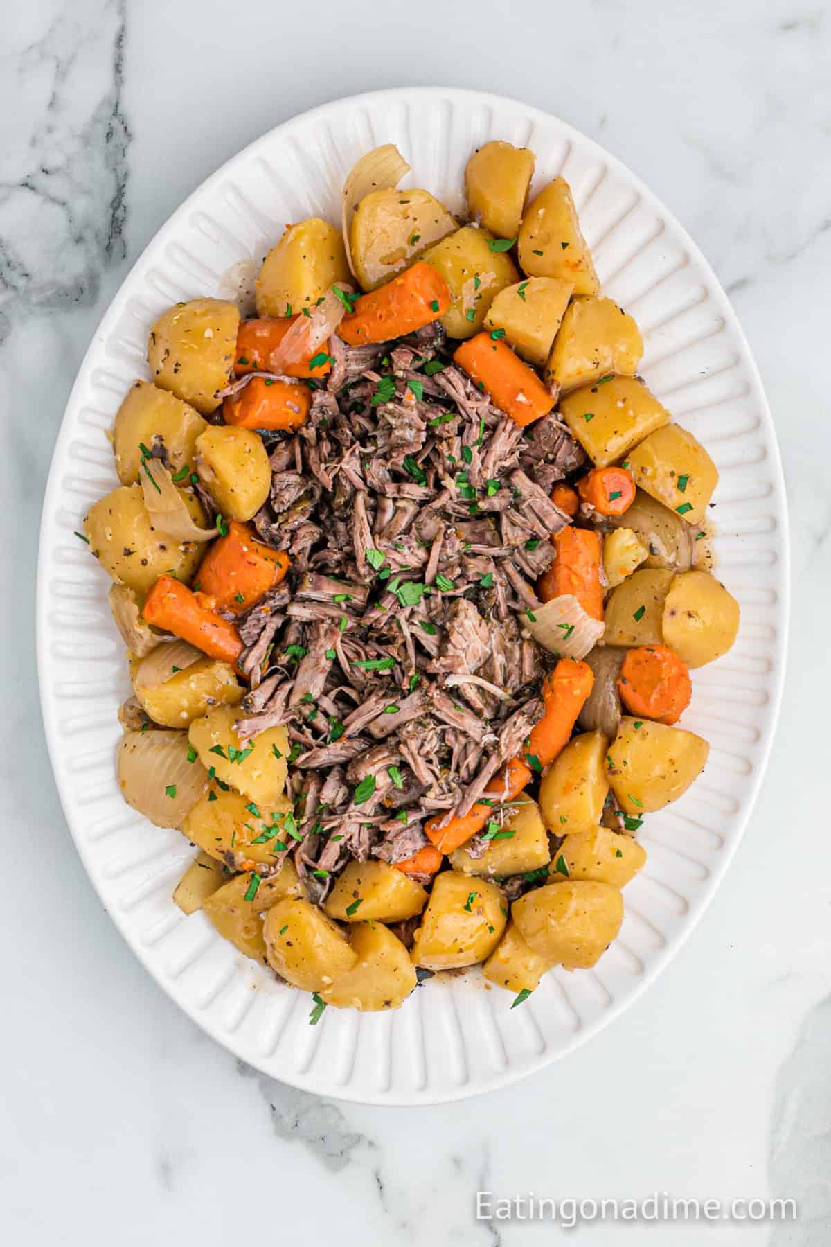 Shredded roast on a platter surrounded by cooked potatoes and carrots.