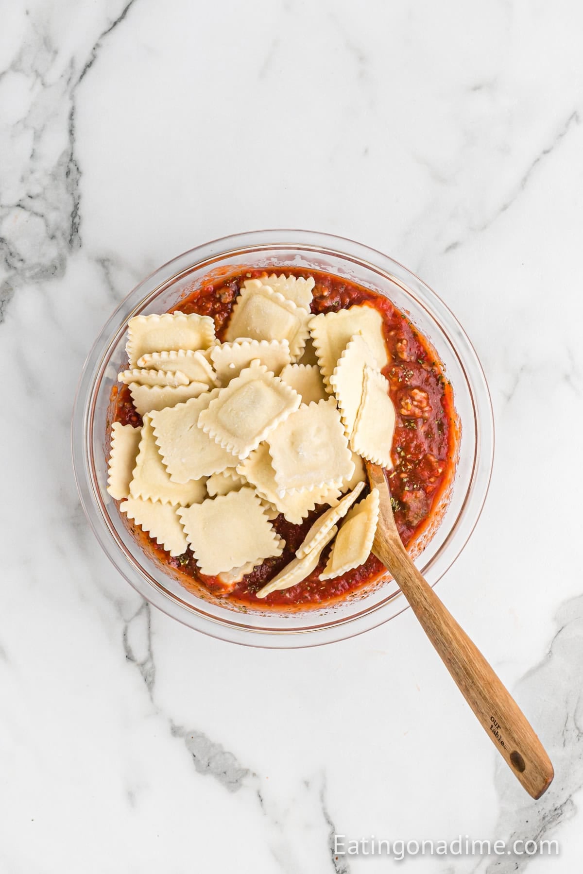 Ravioli added to the sausage and sauce mixture in a bowl with a wooden spoon.