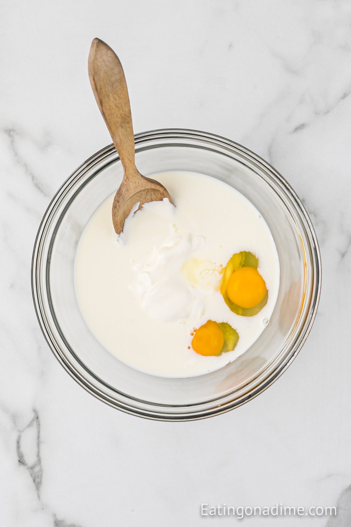 Sour cream, milk and eggs combining together in a bowl with a wooden spoon.