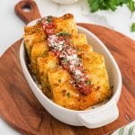Four golden, crispy Olive Garden Fried Lasagna ravioli topped with marinara sauce and grated cheese, garnished with chopped parsley, served in a white oval dish on a wooden board.