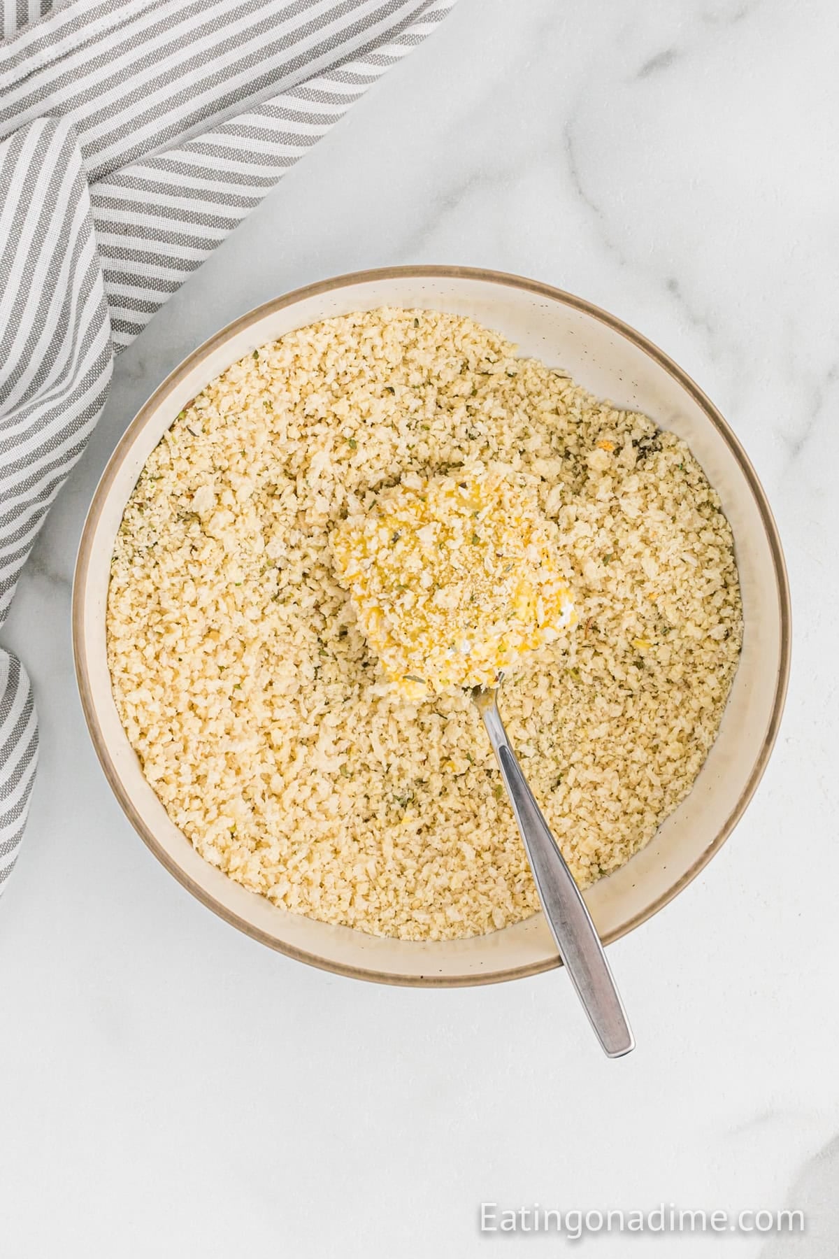 Uncooked ravioli covered in breadcrumb mixture in a bowl.