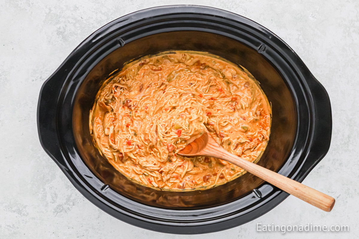 Queso chicken mixture in the slow cooker with a wooden spoon