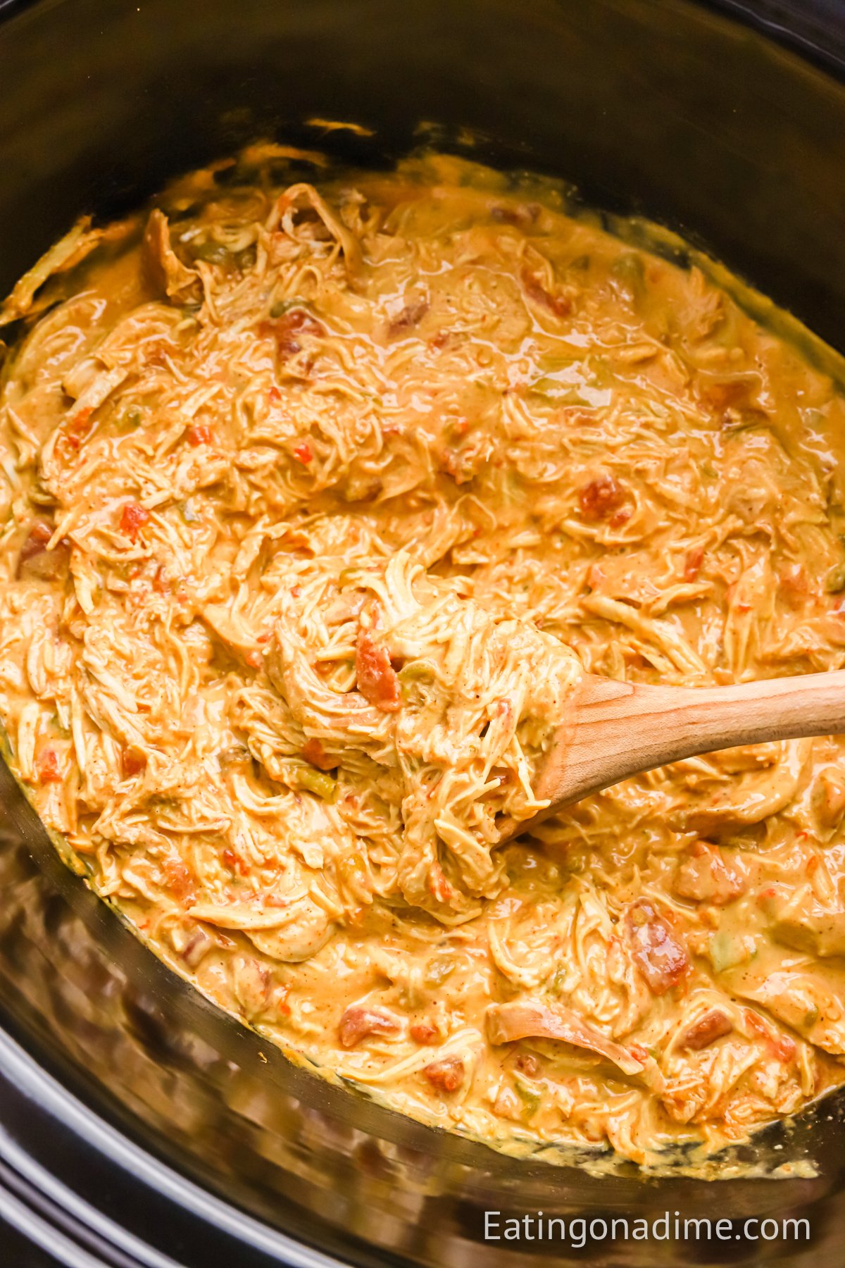 Queso chicken mixture in the slow cooker with a wooden spoon