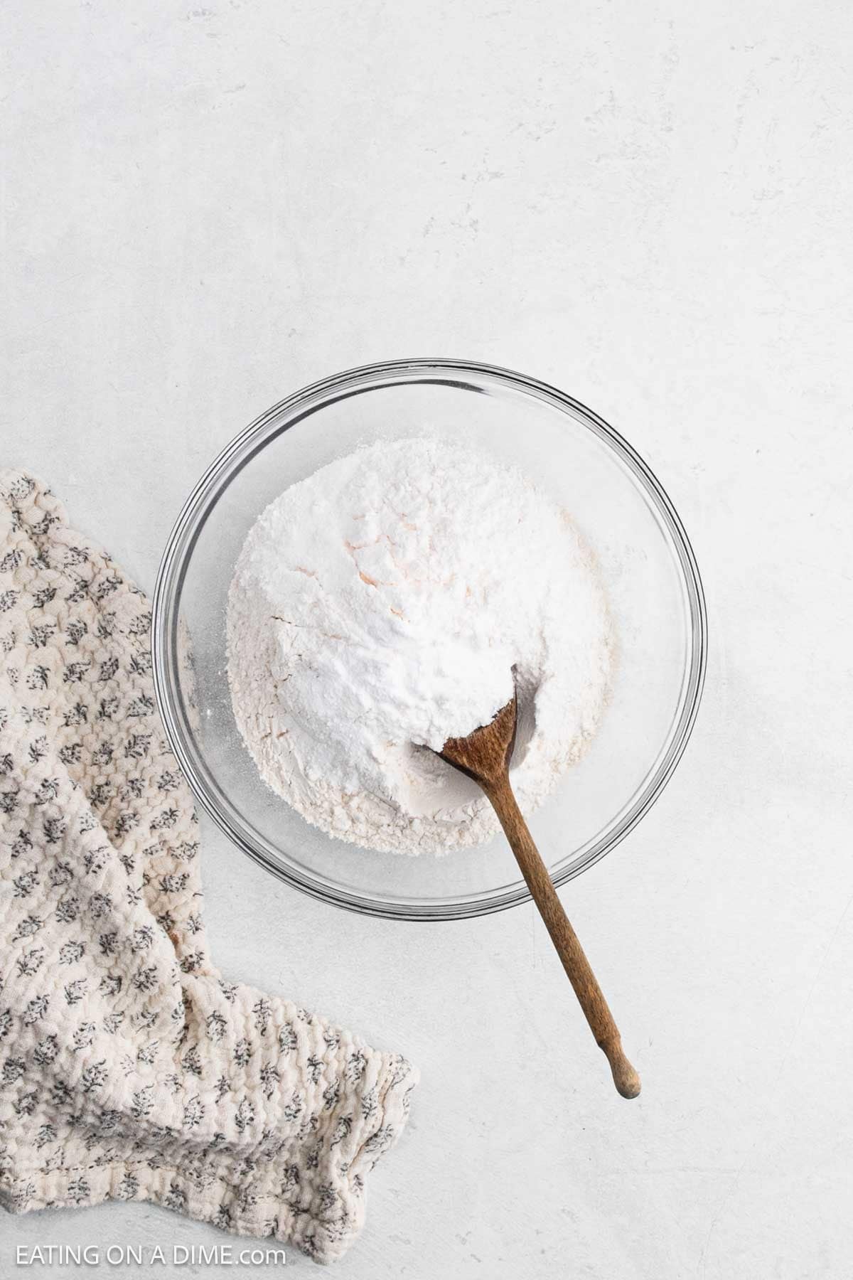 Flour, baking soda, and salt are placed in a bowl with a wooden spoon.