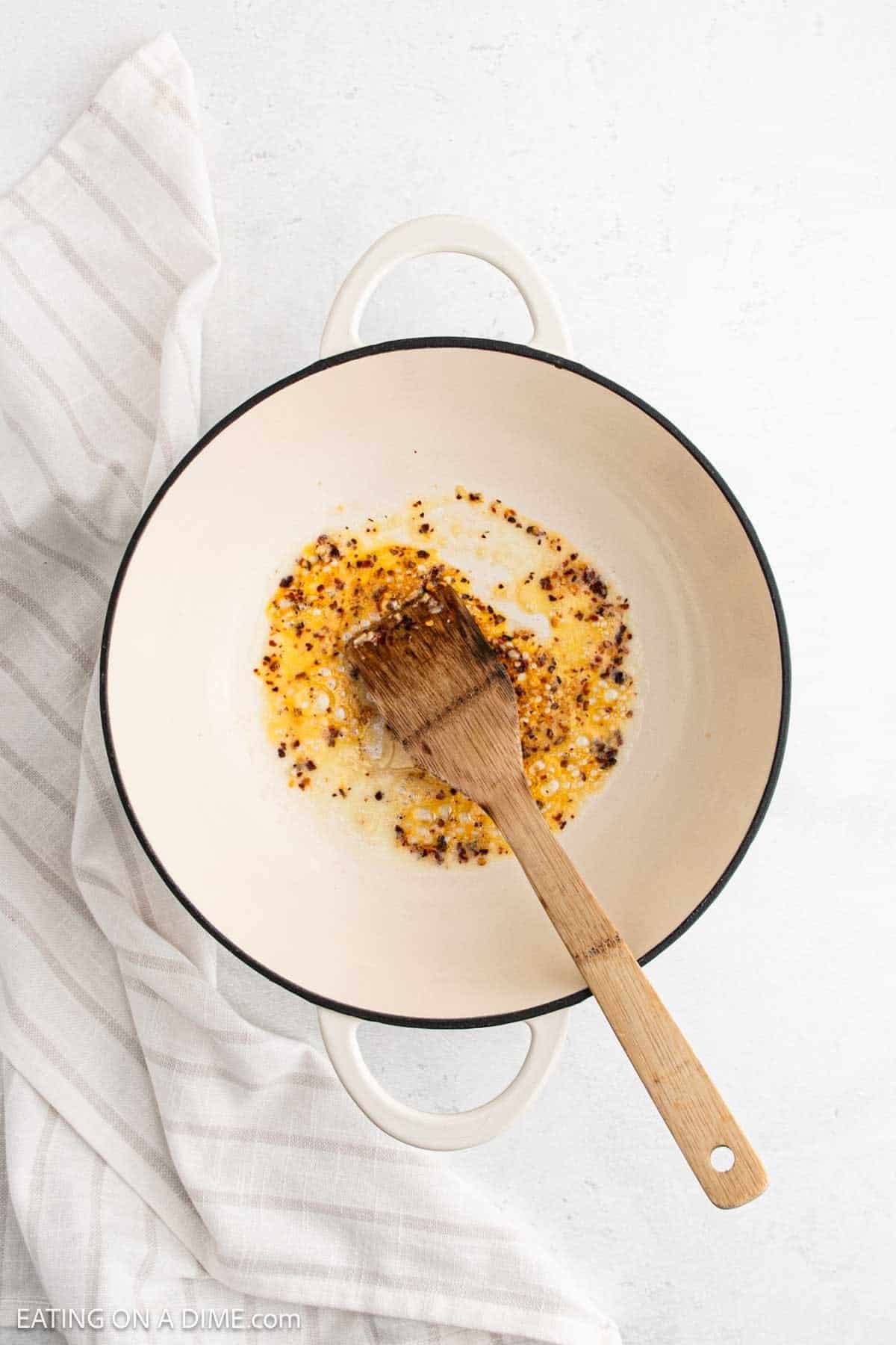Cooking melted butter with minced garlic and red pepper flakes in a large pot with wooden spoon