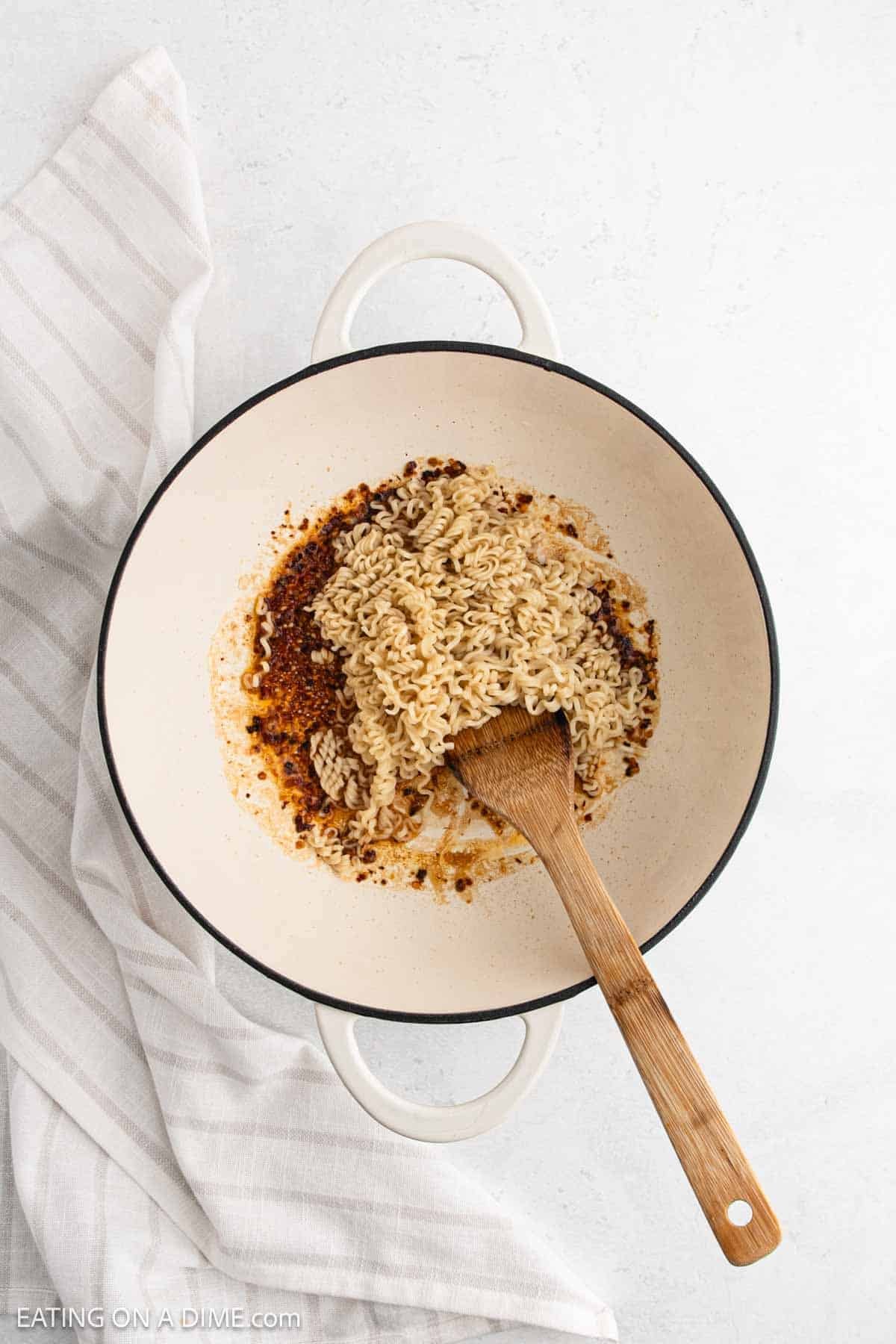 Adding the ramen noodles to the red pepper flakes mixture in a large pot with a wooden spoon