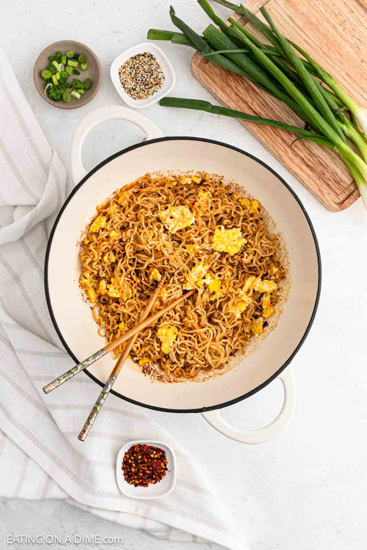 Large pot of Ramen Noodles with large pieces of scrambled eggs with small bowls of green onions and seasoning mixture and fresh green onions