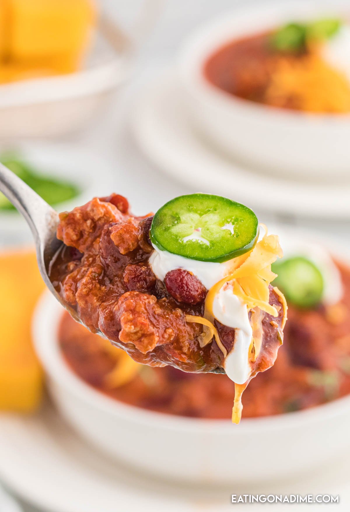 Turkey Chili in a bowl topped with cheese, sour cream and jalapenos in the background with a bite on a spoon