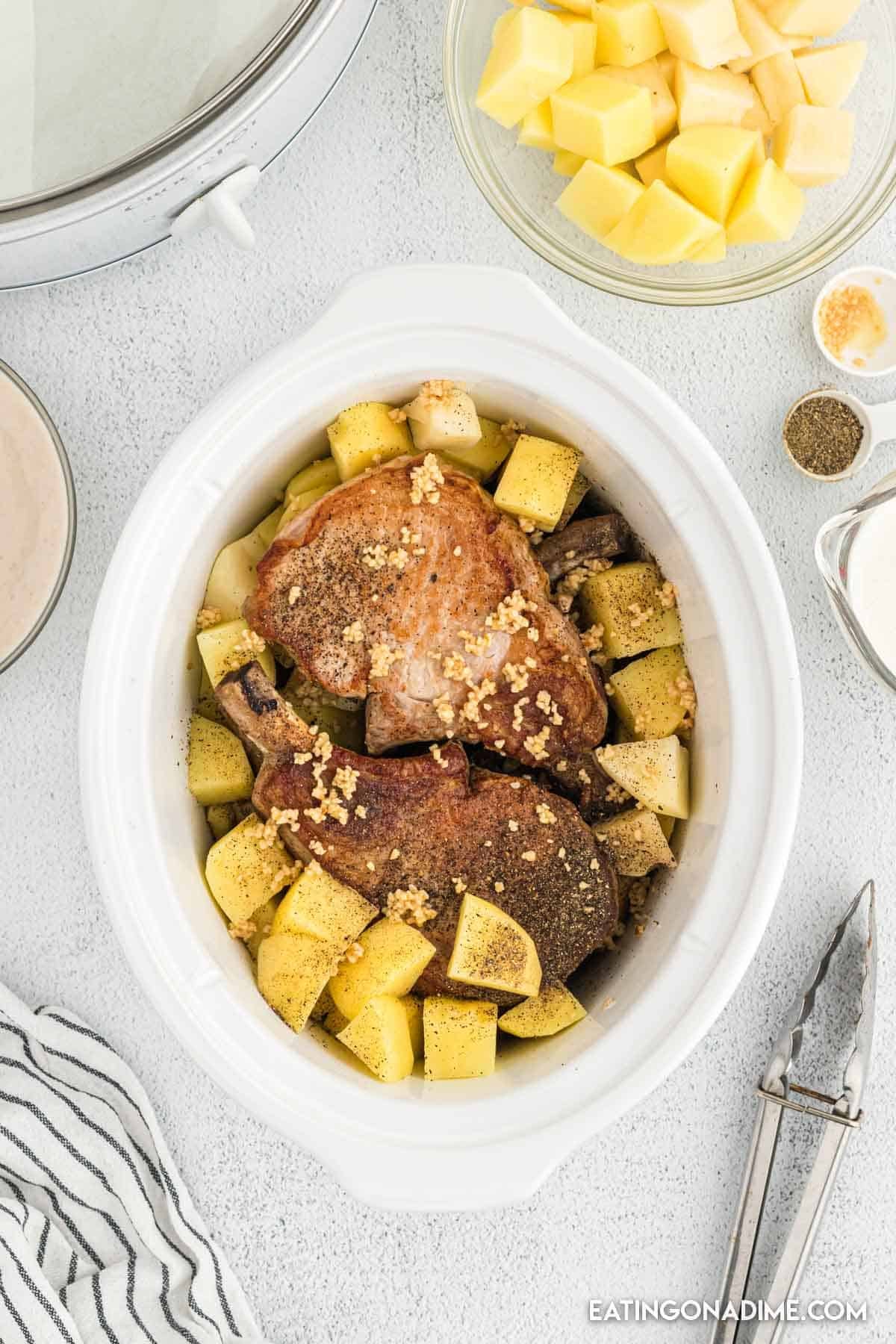 Seared pork chops in the slow cooker with potatoes and topped with minced garlic and spices.