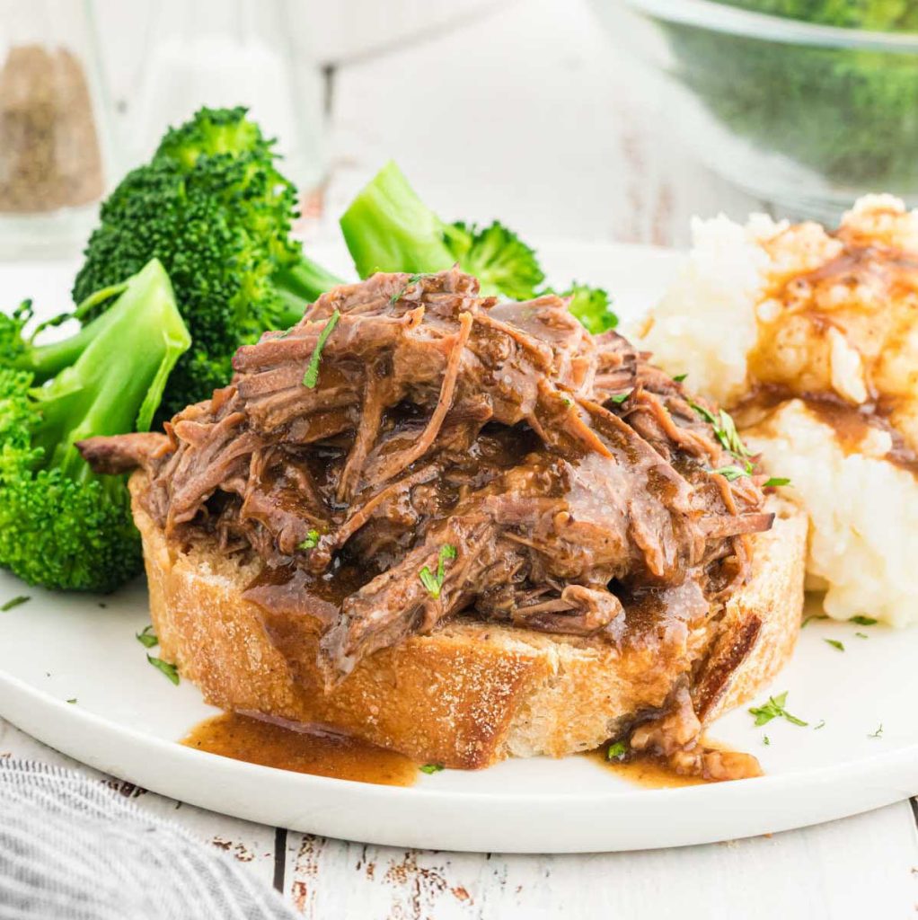 Shredded Roast Beef Sandwiches on a plate with a side of broccoli and mashed potatoes and gravy