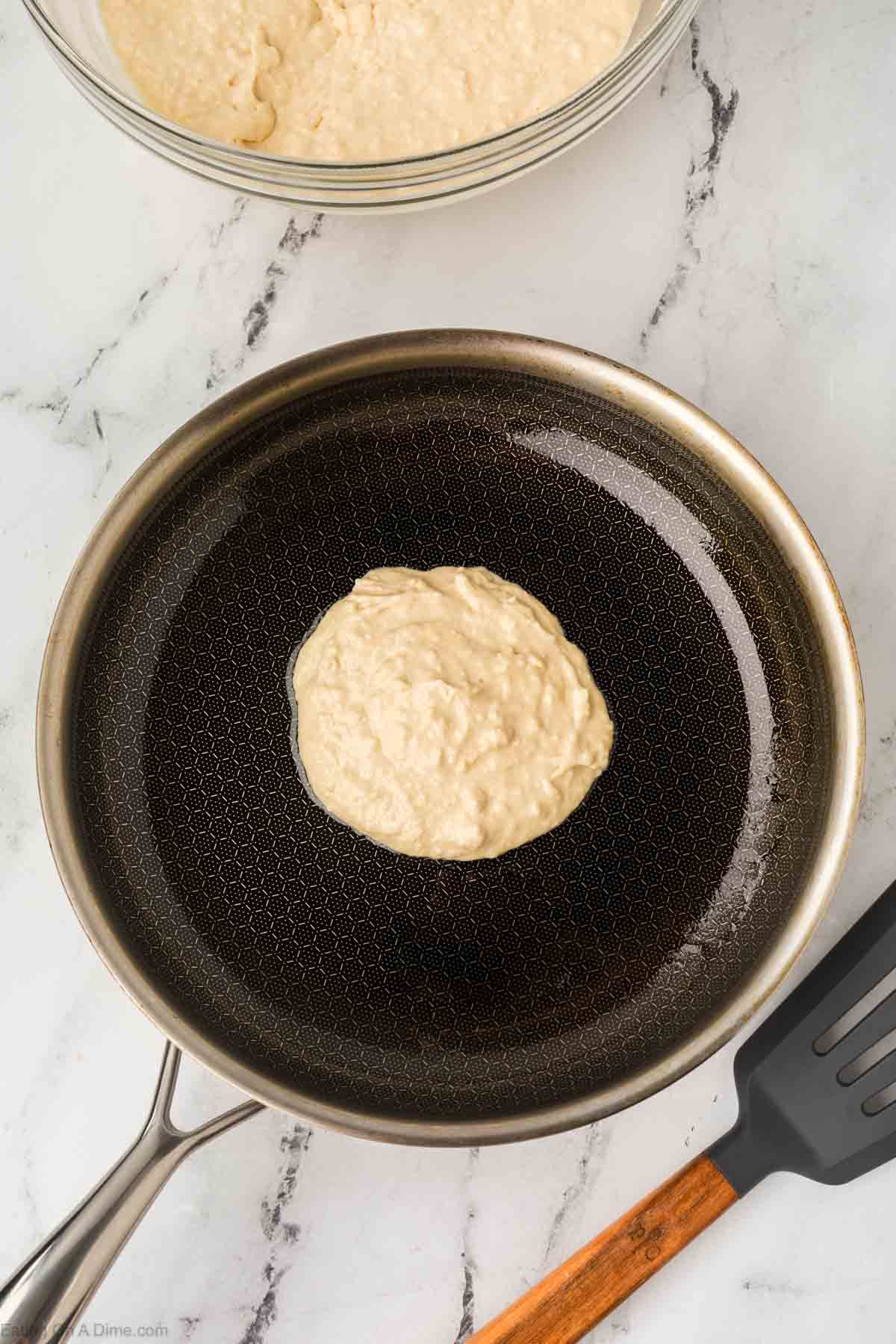 Pouring pancake batter in the pan with a bowl of the pancake batter on the side