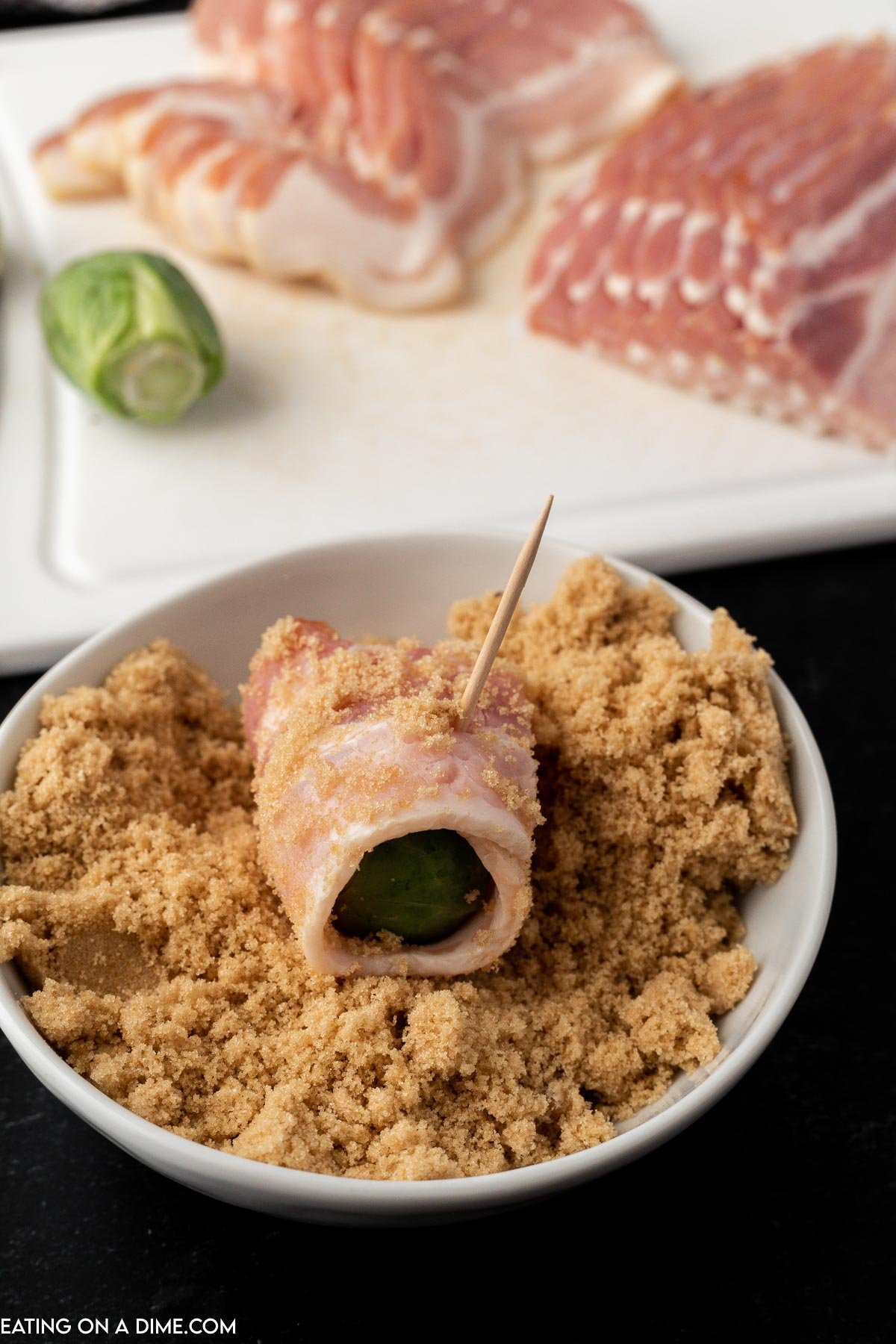 Bacon Wrapped Brussel Sprouts uncooked being dipped in brown sugar