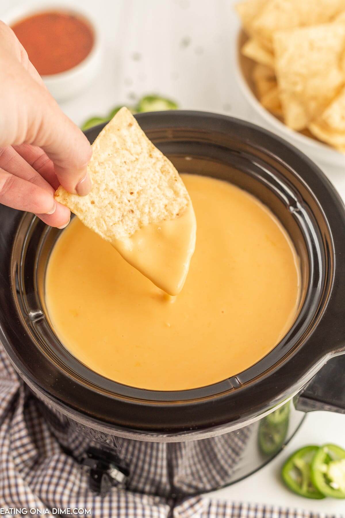 Nacho Cheese Dip in the slow cooker with a chip being dipped in